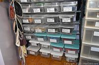 Stacked clear plastic containers labeled with various ballet slipper colors and other pairs of women's shoes, showing storage method and shoe count in lot