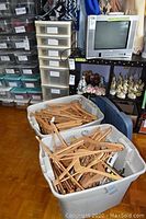 Two large gray plastic totes filled predominantly with wooden hangers, some plastic hangers.