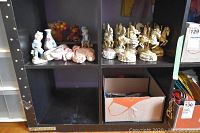 Shelf with ceramic figurines and small sculptures, some painted and some in soft pink tones, assorted knickknacks on display.