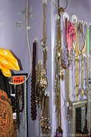 Photo showing several costume necklaces and pendants hanging on white wall hooks with varied bead strands and chains.