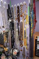Photo showing multiple necklaces hanging side by side on wall hooks, colors include black, brown, yellow, white, and mixed colors.