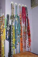 Full view of multiple costume jewellery necklaces hanging on a wall-mounted hook. Various colors and styles visible, mainly beaded.