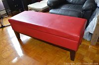 Red vinyl storage bench with wooden legs and visible seating surface.