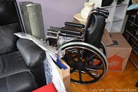 Folded chrome Airgo ProCare IC wheelchair beside couch
