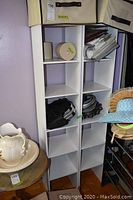 Full view of two white narrow shelving units side by side with various items on shelves.