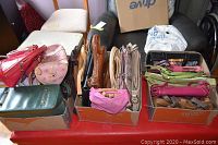 Three boxes filled with assorted handbags in various colors and materials placed on a red surface.