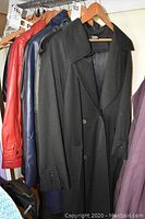 Four coats hanging on a rack including a red leather coat, blue leather jacket, black overcoat, and mauve trench.