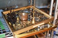 Gold framed mirror and various brass and copper decorative items including a dinner bell, napkin rings, candle snuffer, and figurines on a glass surface.