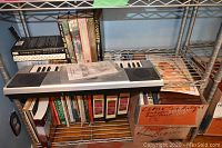Metal shelf with battery operated electronic keyboard on middle shelf, books on top and bottom shelves.