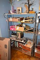 Metal wire shelf loaded with various items including boxes, books, keyboard, and glassware.