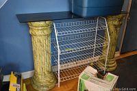 Wide angle showing full table setup with two yellow decorative mantle-style columns, black rectangular top, and white metal wire shoe rack beneath