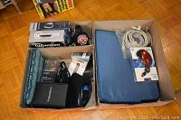 Wide shot showing two boxes containing electronics and accessories including headphones, Blackberry boxed device, cables, and Acer laptop charger.