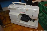 Full view of the white Singer sewing machine with handle on top and foot pedal cord visible.