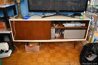 Full front view of console cabinet showing painted body, sliding veneered door, open shelf with electronics and overall shape