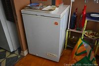 White chest freezer placed in kitchen corner near doorway with visible surrounding items including plates on top.