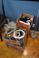 Three cardboard boxes stacked with various electronics and cables. One box labeled 'Phones & Commt Radio'.