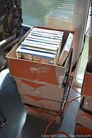 Four stacked cardboard boxes filled with VHS tapes in storage area, showing wear on boxes and tapes.