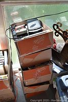 Stack of six cardboard boxes filled with VHS tapes positioned by a window on wooden floor.