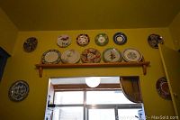 Wall display of 12 decorative collector plates arranged above a door frame on a yellow wall, showing variety of designs including floral and geometric patterns.