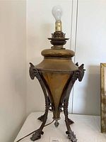 Full view of the brass oil lamp showing conical body, ram's head details, and electrified bulb socket on top.