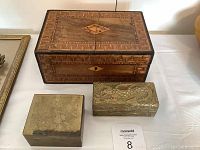 Front and top view of all three boxes showing inlaid wooden jewelry box with geometric patterns, Asian brass box, and brass repose dragon box