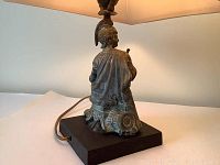 Side and back view showing metal Roman soldier figure seated with detailed armor, cape, and helmet on black base with electrical cord.