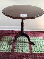 Front view of the walnut tilt top table showing round scalloped edge and three-legged pedestal base.