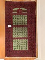Full view of the carpet laid flat showing central green panels with repeated motifs and red borders.