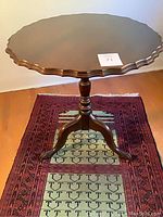 Side table with tilt top and scalloped edge on a red and green patterned rug