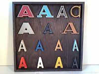 Photo of entire vintage collection showing 15 metal letter A's in various colors and styles mounted on a wooden board.