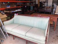 Front view of the light green sofa showing the full seating and wooden frame with carved details.
