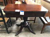 Full view of rectangular wooden flip top table with dark finish and brass claw feet on pedestal base, showing scratches on surface.