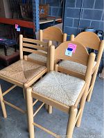 Four wooden barstools with woven thatched seats and two different styles of backs, shown from angle.
