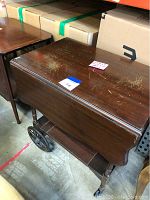 Wooden tea cart showing the drop leaf top, wheels, and lower shelf.