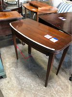 Wooden side table with a curved front edge and four legs, placed among other furniture items.