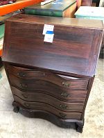 Front view of the closed four drawer wooden secretary with fold-down desk, showing curving drawer fronts and brass handles.