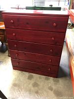 Frontal view of the chest showing the five drawers with round wooden knobs and the red stained pine finish.