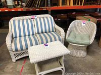 White wicker loveseat, chair, and table. The loveseat has blue and white striped cushions. The chair has a green cushion. The table is rectangular with a shelf underneath.