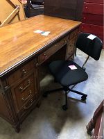 Photo showing the front side of the wooden desk and the black rolling chair positioned beside it.