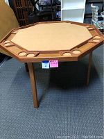 Octagonal wooden folding game table showing integrated cup holders around the edge and a felt-like playing surface.