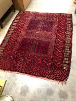 Full view of the red area rug showing its overall pattern and condition on a concrete floor.
