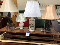 Four assorted table lamps on a wooden surface showing variety in style and colors.