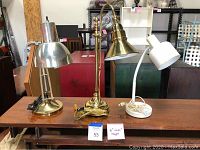 Photo showing all three metal desk lamps on a wooden surface, displaying their varying height, design, and finish.