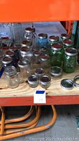 Photo of assorted canning jars of various sizes and colors, showing green, blue, clear, and purple glass jars with lids on a shelf.