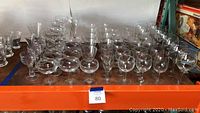 Wide view showing multiple rows of assorted clear stemware glasses including various bowl and rim shapes.