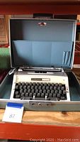 White Signature 440T manual typewriter inside blue-gray carrying case on shelf.