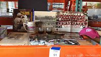 Display of Redskins memorabilia including large black and white team photo, 1982 championship team photo, glass mugs, coasters, newspapers, posters, and a pink baseball cap.