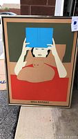 Framed Will Barnet poster displayed upright outdoors, showing stylized figure with cat and blue object