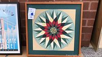 Full view of the framed geometric wooden artwork in wood frame with green mat and star pattern design in center.