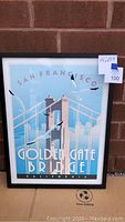 Photo of framed San Francisco Golden Gate Bridge artwork against a brick wall, showing full artwork and frame.